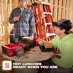 Workers eating at a wooden spool table with an open M18 Jobsite Lunch Warmer on a construction site.