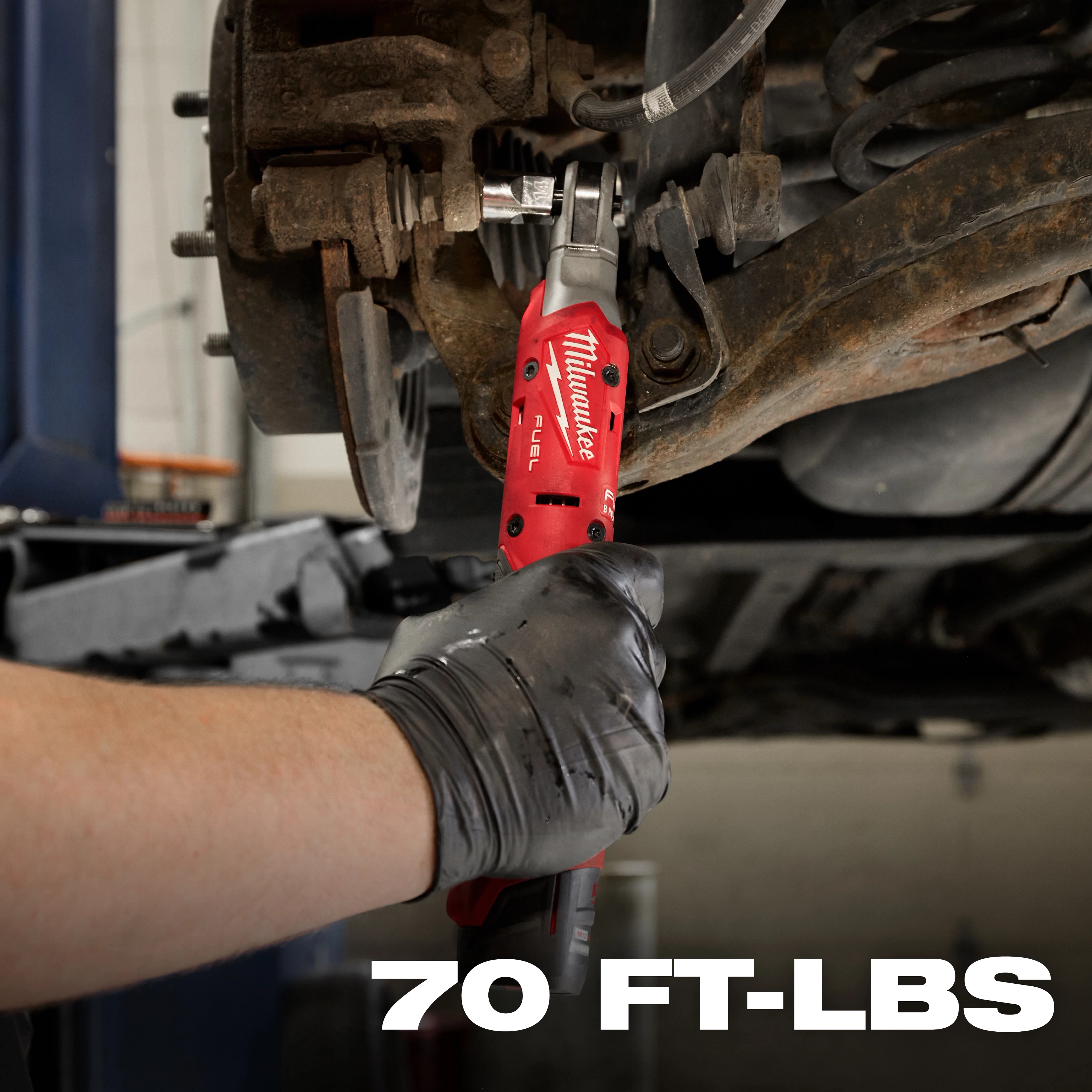 A person uses the red Milwaukee M12 FUEL™ 3/8" Ratchet to work on a car's suspension system. The tool's display shows it can produce up to 70 foot-pounds of torque.