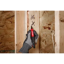 A gloved hand using the INKZALL Double-Sided Black Jobsite Marker. Fine Point & Chisel Tip to write markings on a wooden beam. The pen is used in construction settings for precise marking.
