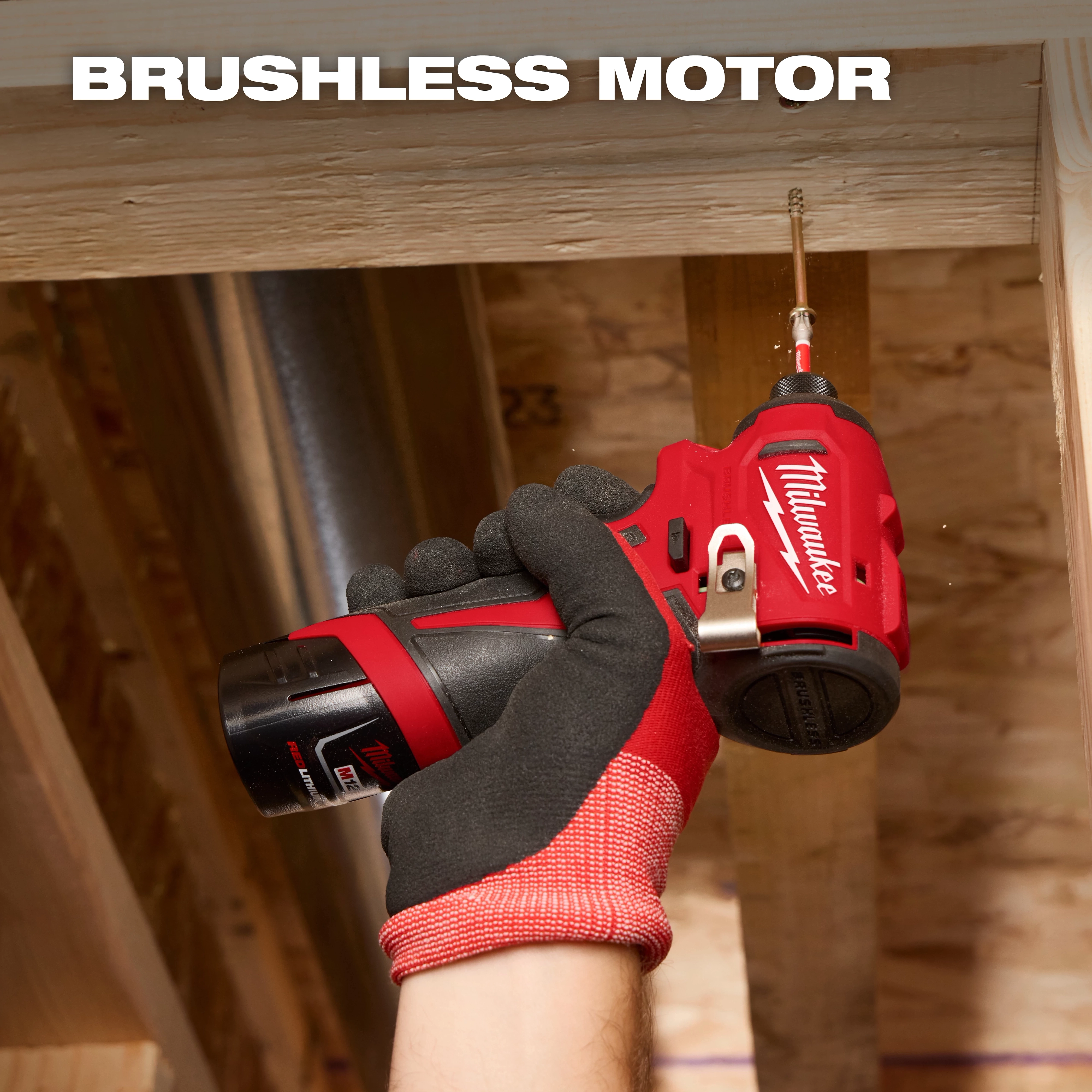 A gloved hand holds a Milwaukee brushless motor drill, screwing a fastener into a wooden beam within a construction area.