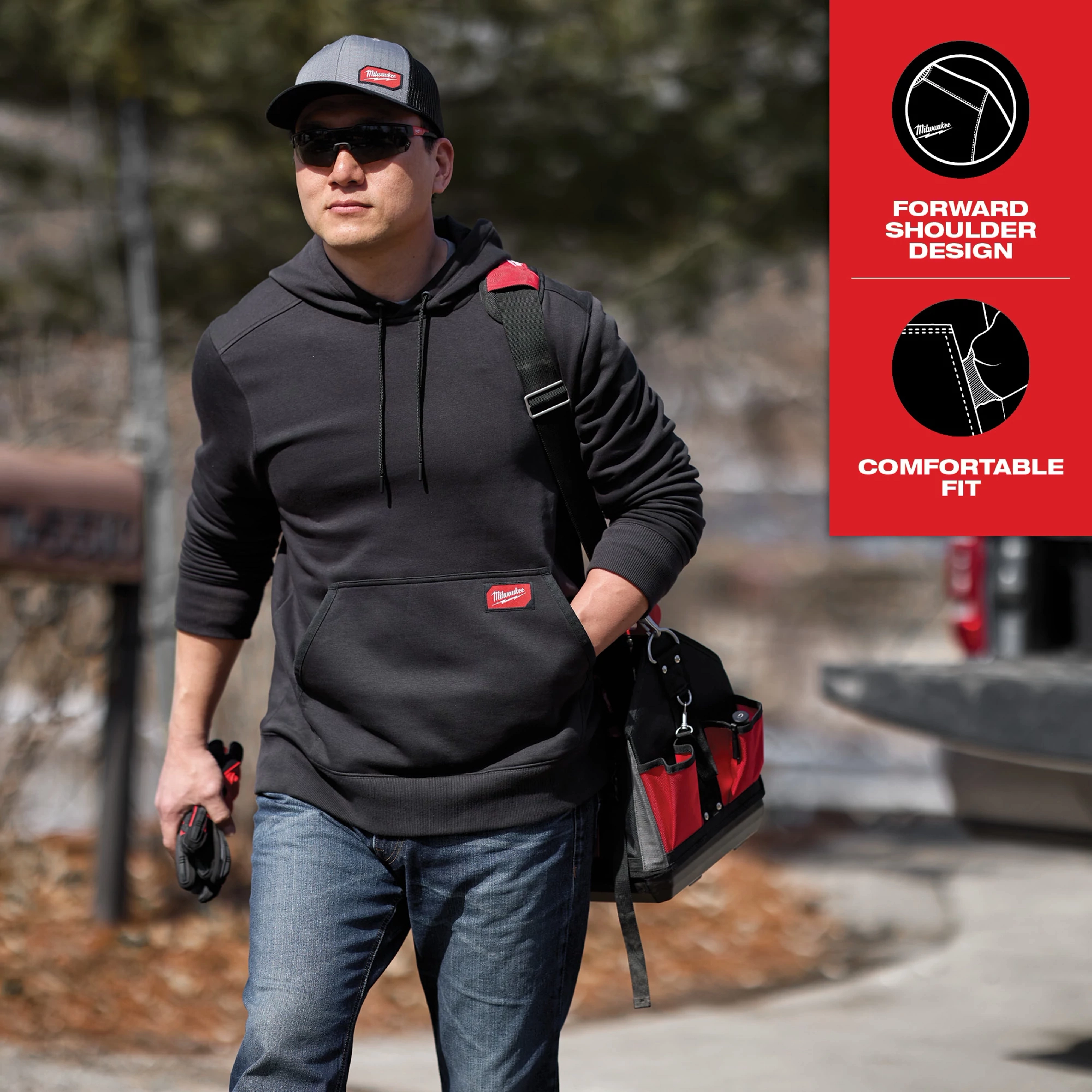Man wearing a black Midweight Pullover Hoodie Feature Shot 3 holds tools and a tool bag, with captions "Forward Shoulder Design" and "Comfortable Fit."