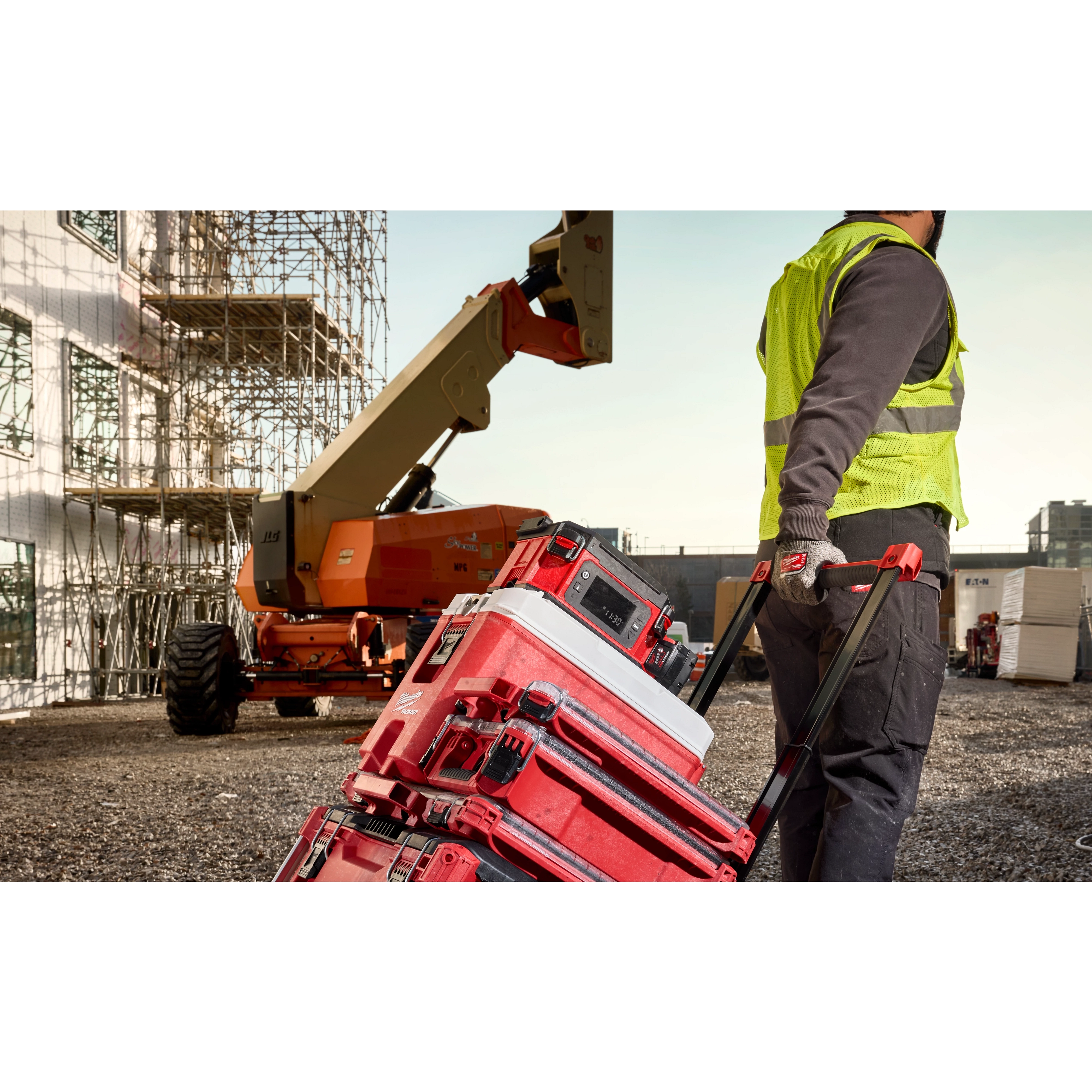 Worker pulling a red stack of toolboxes with the M18 Jobsite Lunch Warmer on top, on a construction site.