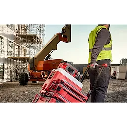 Worker pulling a red stack of toolboxes with the M18 Jobsite Lunch Warmer on top, on a construction site.