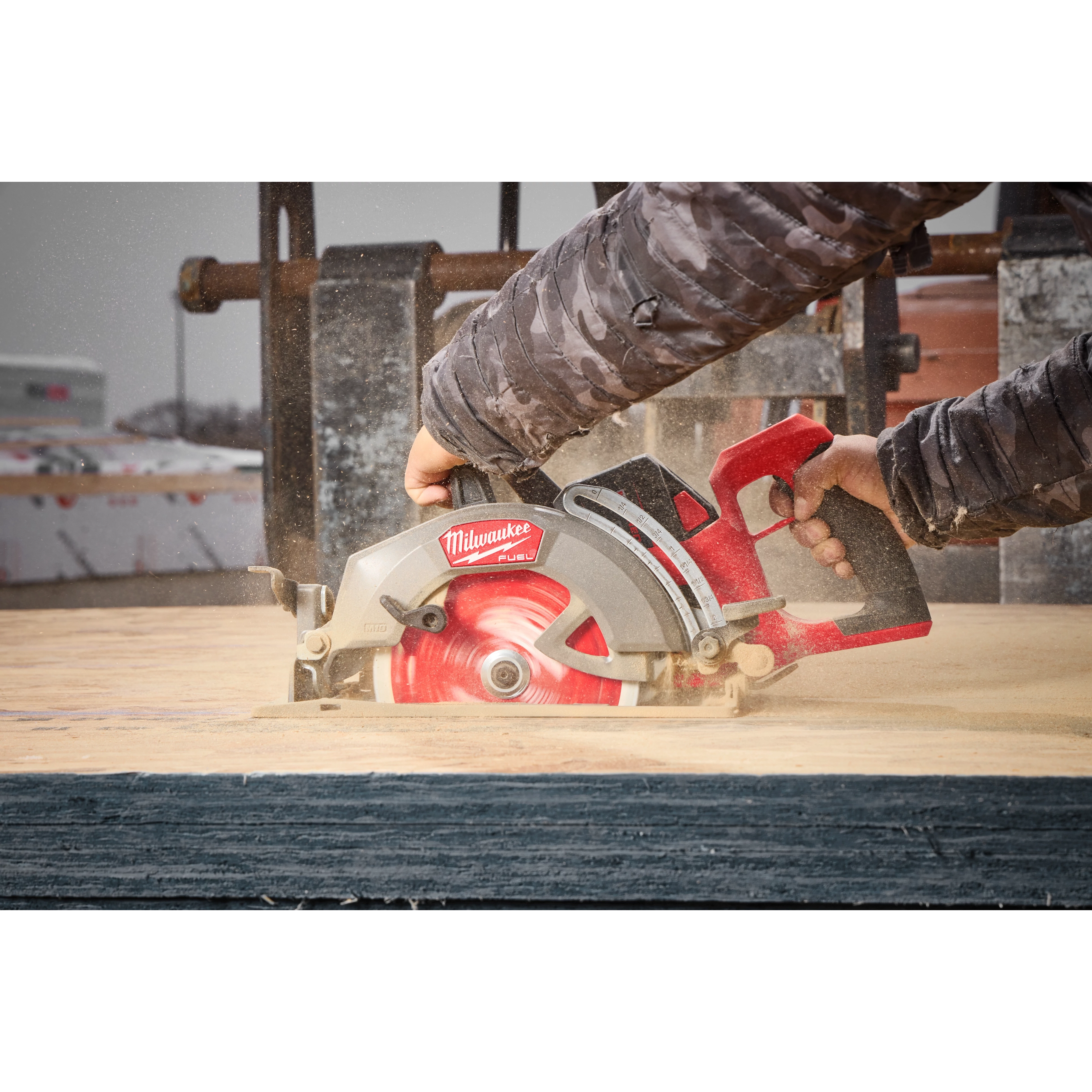 A person is using an M18 FUEL™ 7-1/4" Rear Handle Circular Saw to cut through wood. The saw has a prominent red and silver design with a visible red blade. The operator's hands are securely gripping the saw's handles.