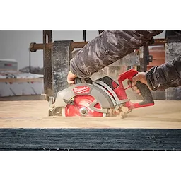 A person is using an M18 FUEL™ 7-1/4" Rear Handle Circular Saw to cut through wood. The saw has a prominent red and silver design with a visible red blade. The operator's hands are securely gripping the saw's handles.