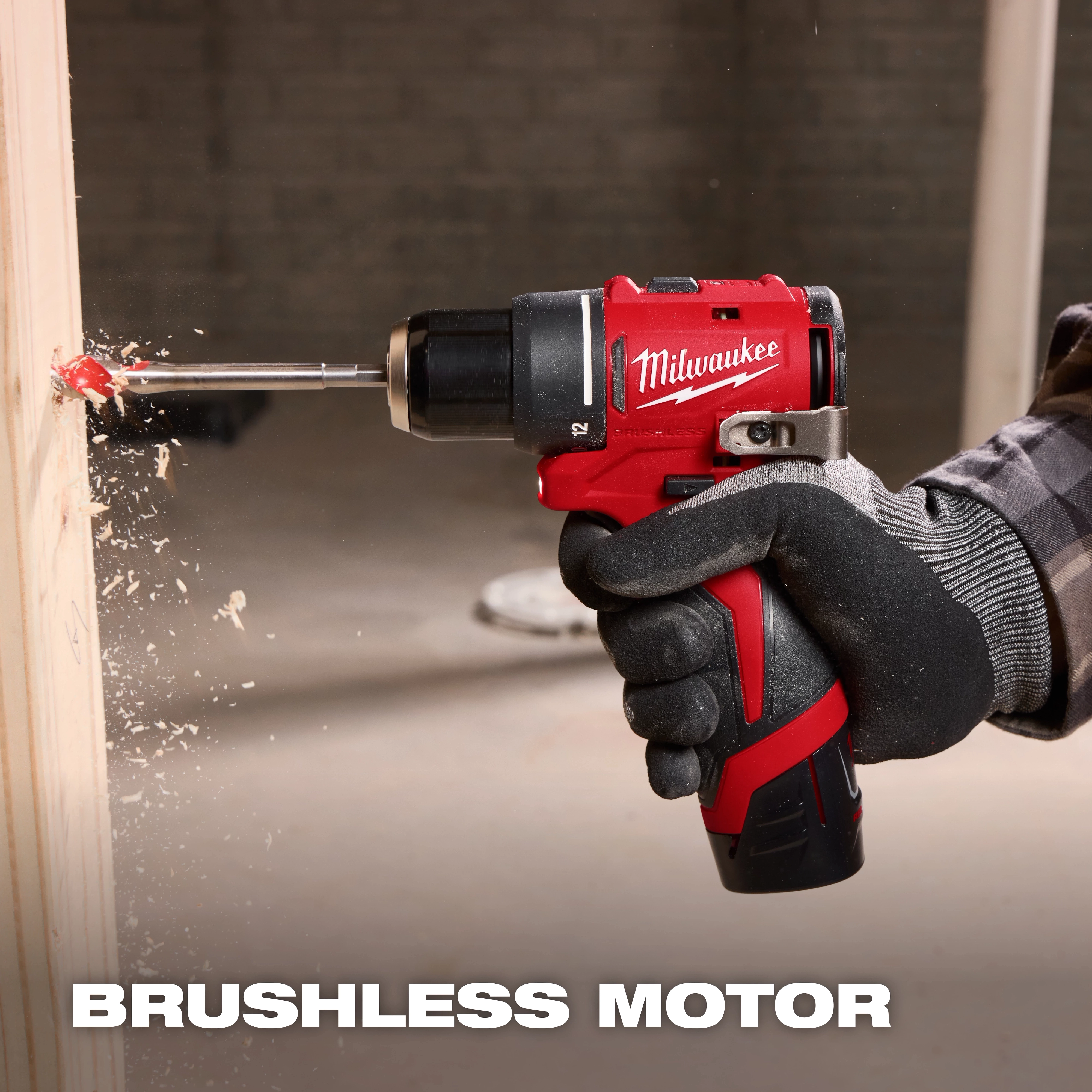 A gloved person uses a red Milwaukee drill with a brushless motor to bore through a light-colored wooden plank, generating wood shavings. The background is blurred, and text reading "BRUSHLESS MOTOR" is at the bottom of the image.