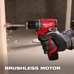 A gloved person uses a red Milwaukee drill with a brushless motor to bore through a light-colored wooden plank, generating wood shavings. The background is blurred, and text reading "BRUSHLESS MOTOR" is at the bottom of the image.
