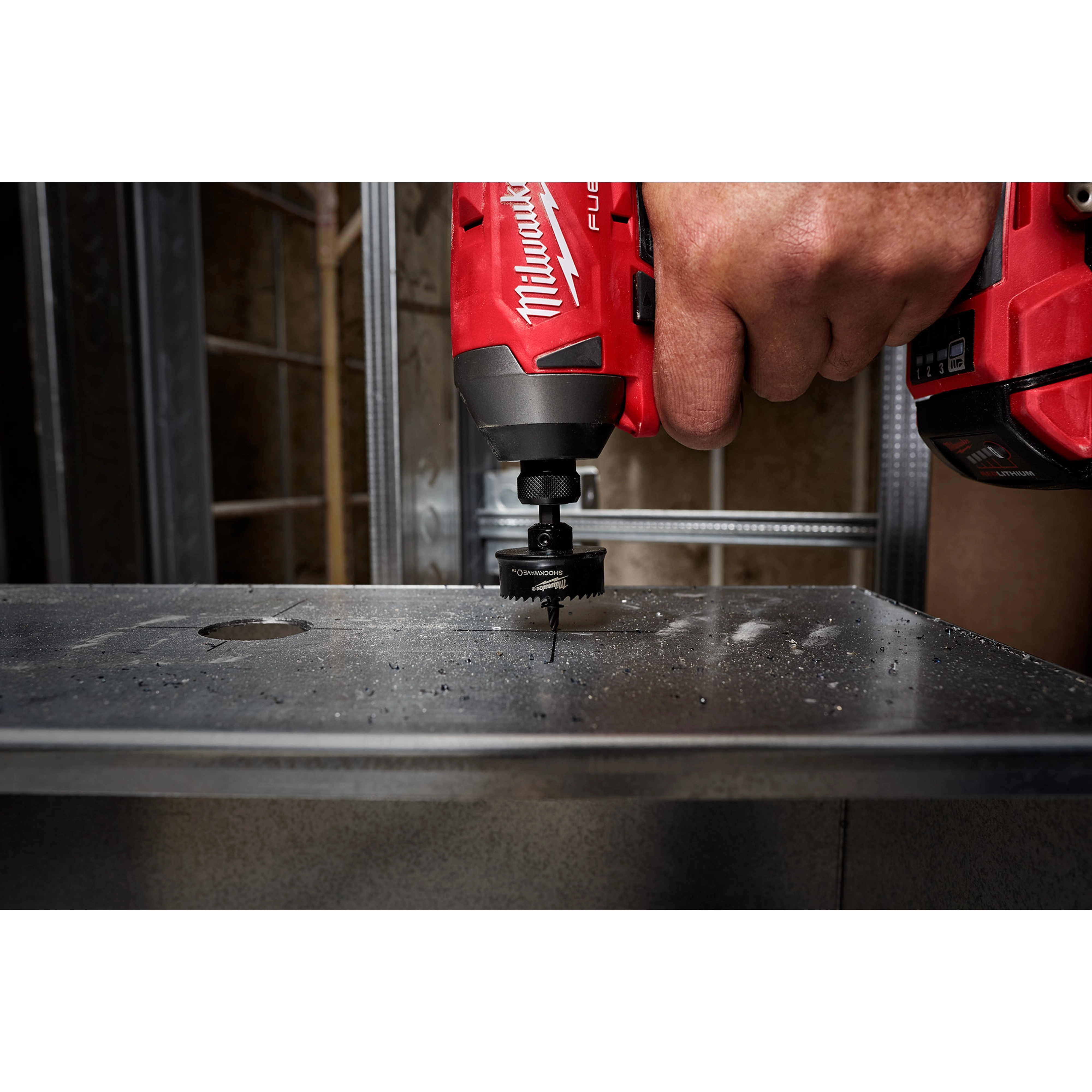 A hand uses a red power drill with a 1-3/8" Shockwave Impact Hole Saw to cut through a piece of metal.