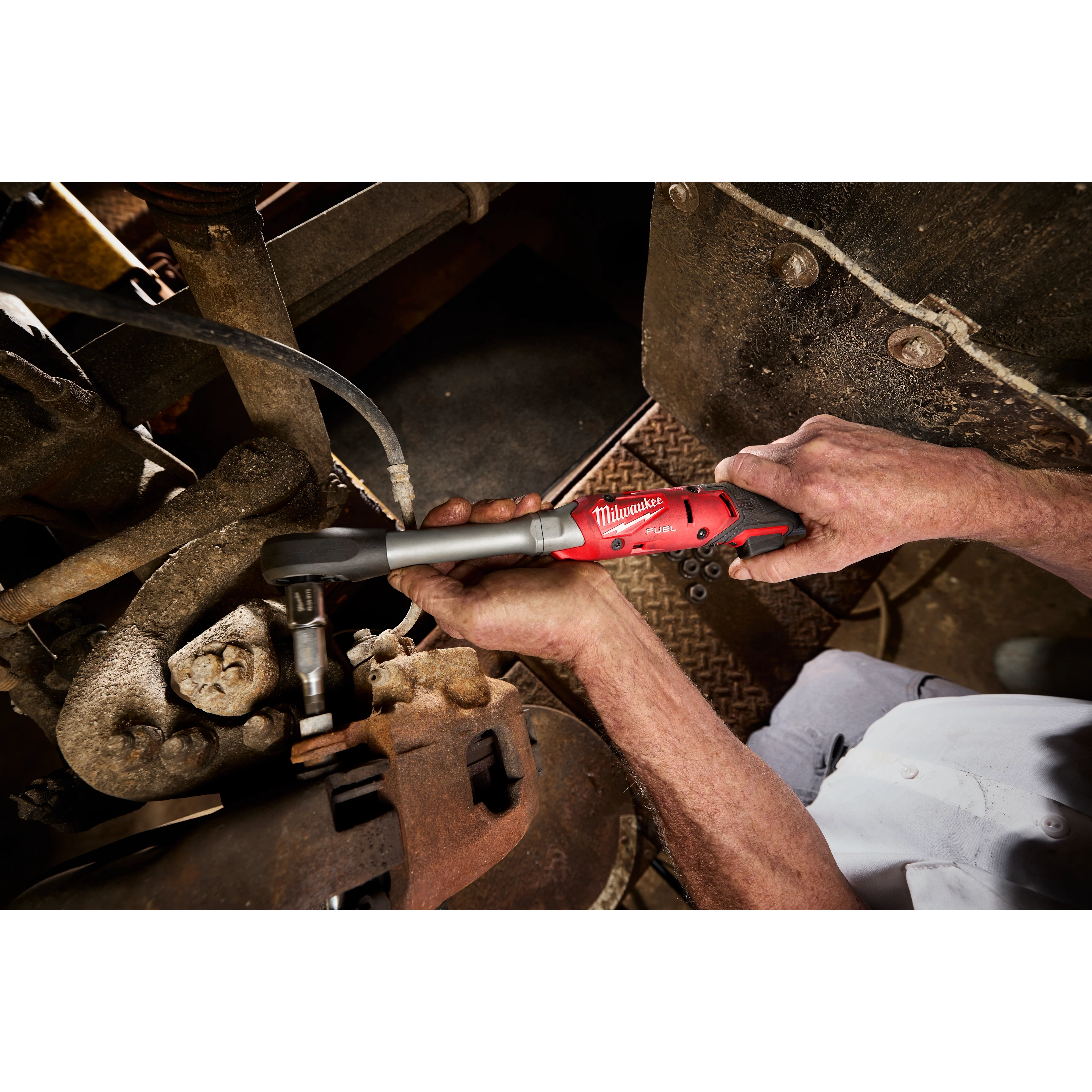 Hands using an M12 FUEL 1/2" Extended Reach Ratchet to tighten a bolt in a metal machinery area.