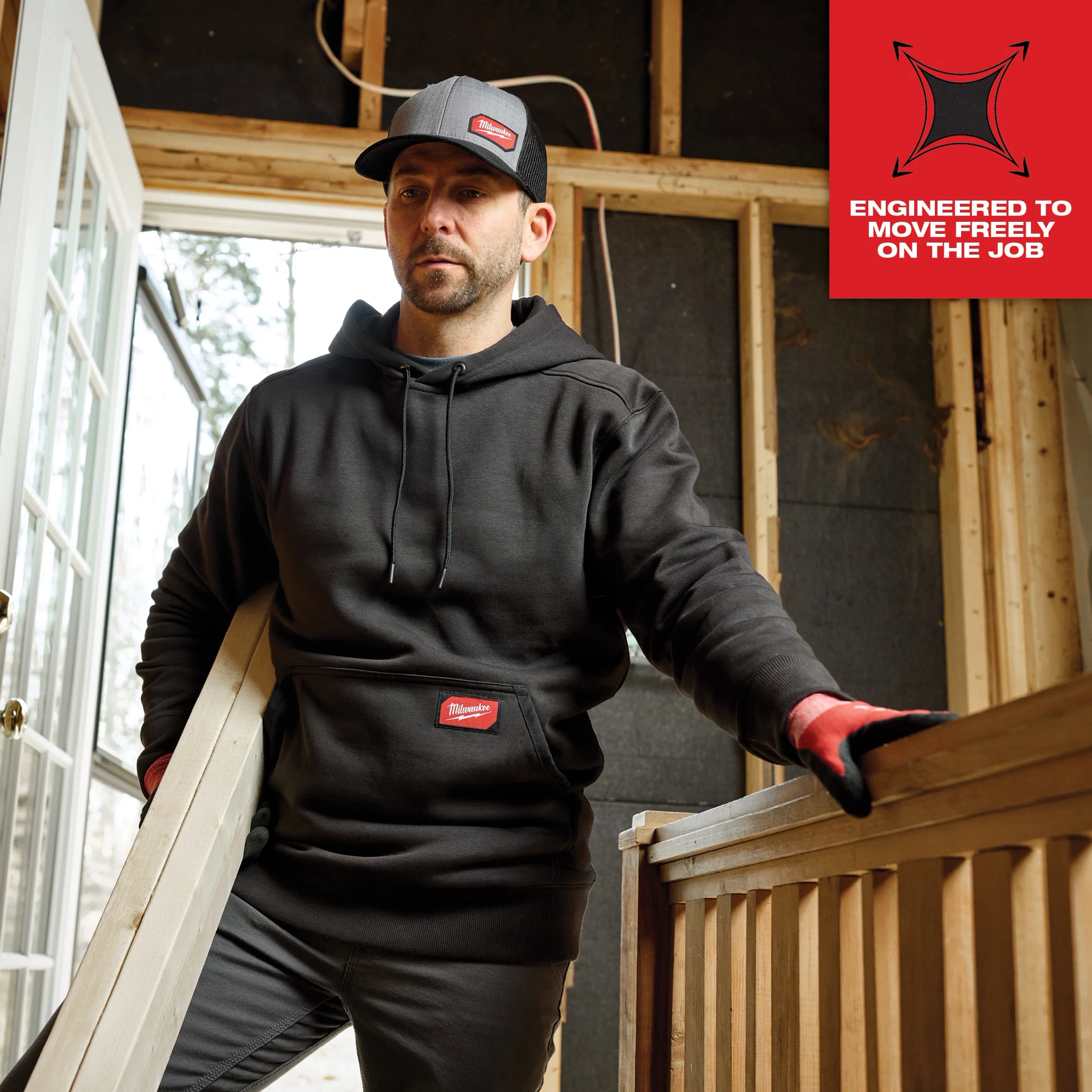 A person wearing a black Midweight Pullover Hoodie Feature Shot 1 is carrying a wooden plank at a construction site.