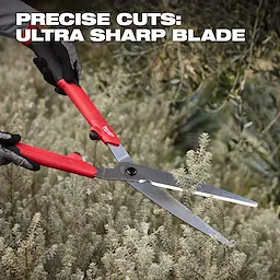 10” Hedge Shears​ with red handles cutting small shrubs in a dense garden area.