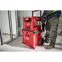 Person standing next to a stack of red PACKOUT XL Crate storage units, equipped with wheels and a handle, in a construction area.
