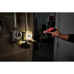A person holds a Dual Range Voltage Detector with LED near an open electrical box. The device is illuminating the inside of the box.