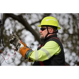 A worker wearing a BOLT™ High Visibility Green Full Brim Safety Helmet – Type 2, Class E operates electrical equipment outdoors. The worker is also equipped with safety gloves and a high-visibility jacket.