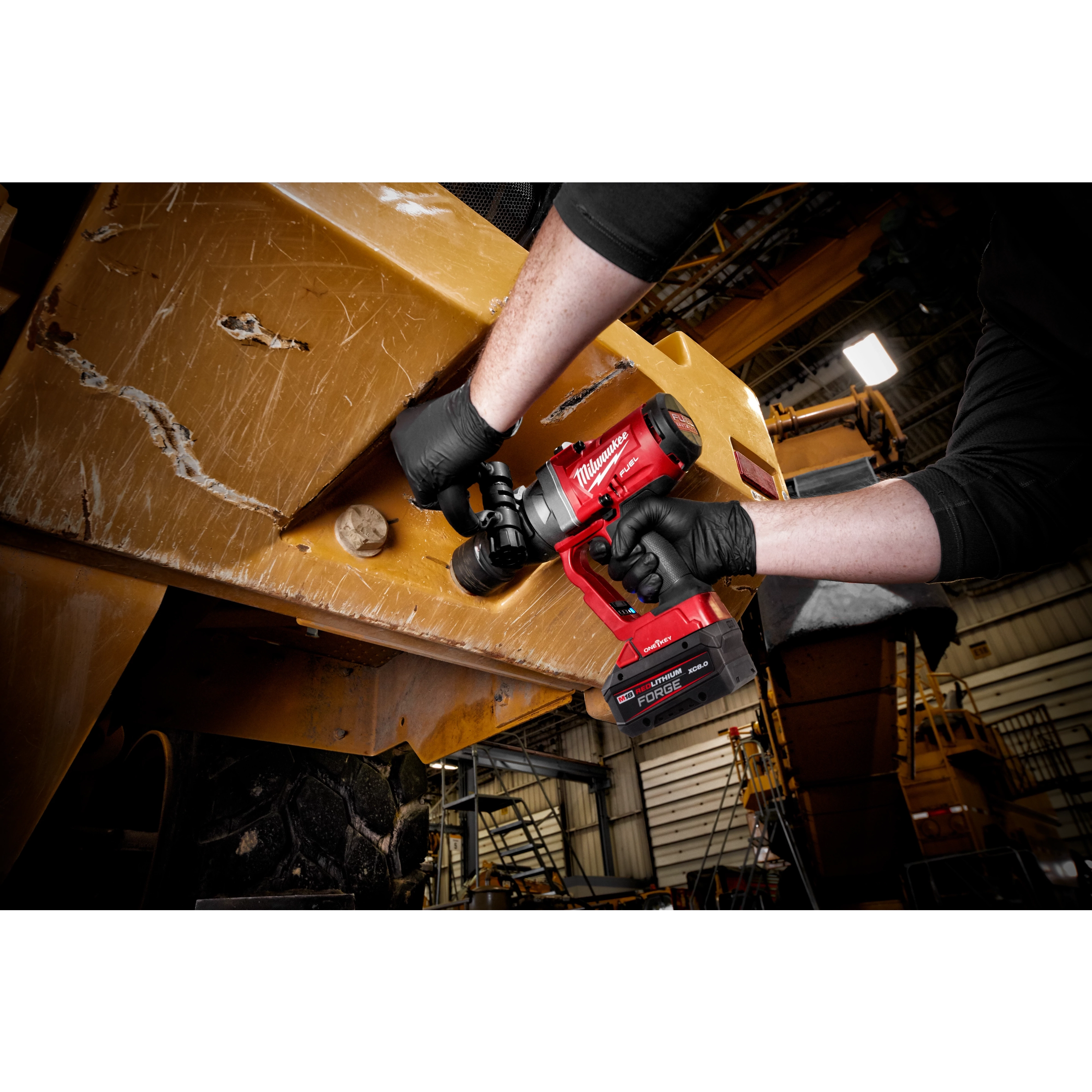 A person using an M18 FUEL w/ ONEKEY 1" High Torque Impact Wrench to work on a large piece of industrial machinery in what appears to be a workshop or factory setting. The tool is bright red, and the person's hands are gloved.