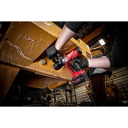 A person using an M18 FUEL w/ ONEKEY 1" High Torque Impact Wrench to work on a large piece of industrial machinery in what appears to be a workshop or factory setting. The tool is bright red, and the person's hands are gloved.