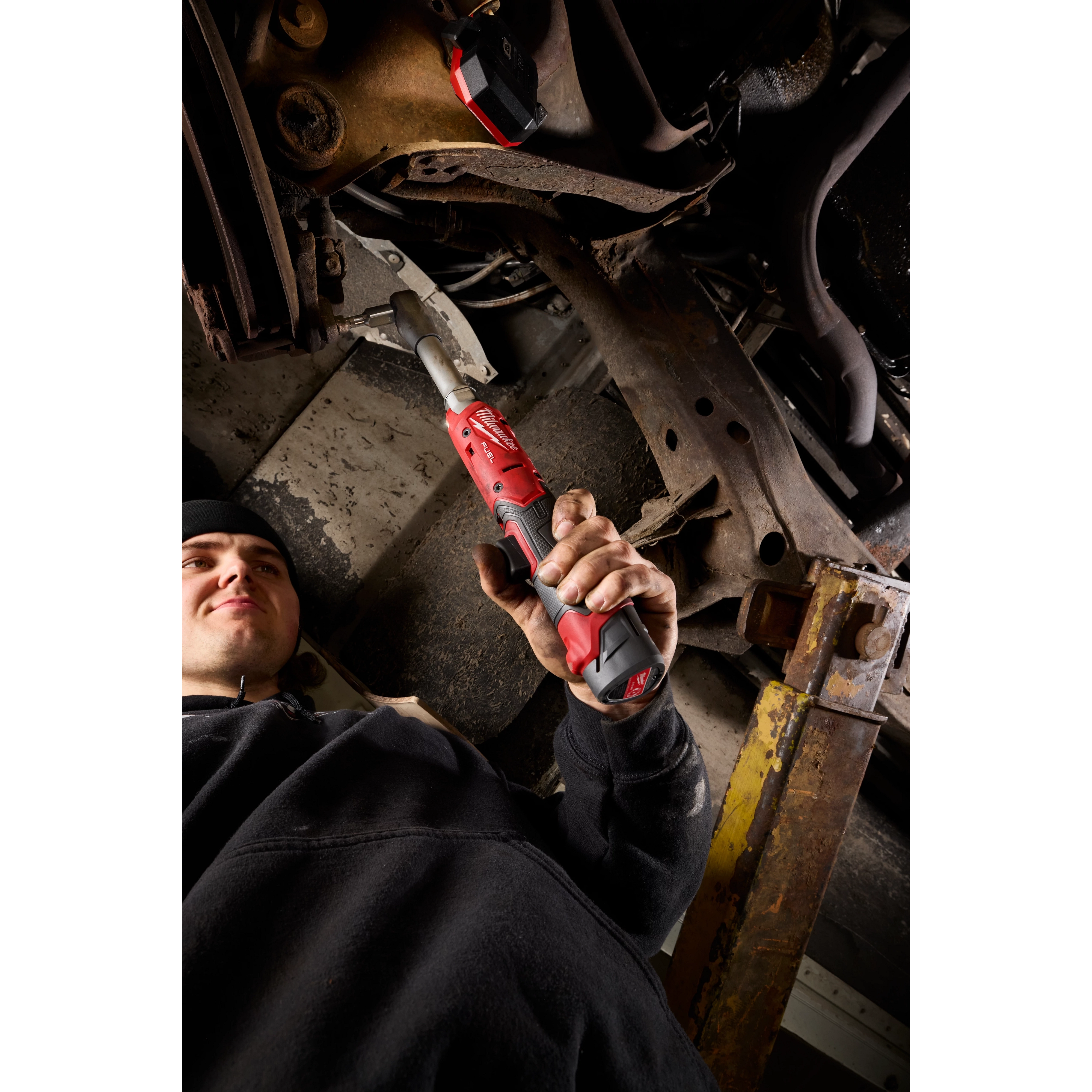 Person using an M12 FUEL 3/8" Extended Reach Ratchet on vehicle undercarriage.